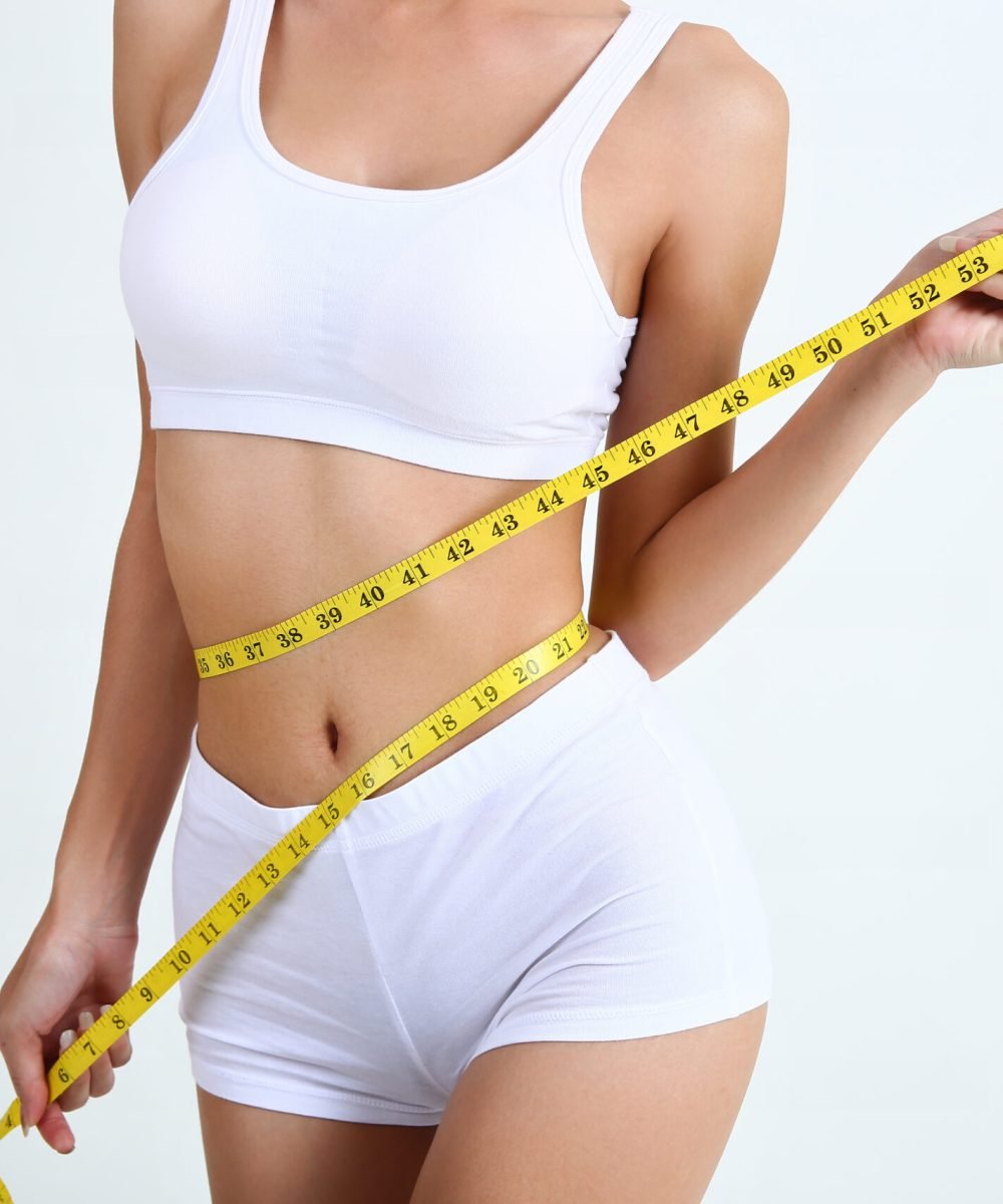 Close up slimming female with beautiful body and measuring her waistline  with measure tape on white background and copy space